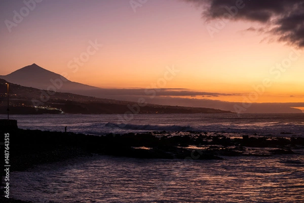 Obraz The sky is dark and the water is calm. The mountains in the background are silhouetted against the sky