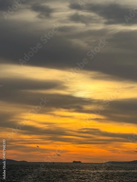 Fototapeta Cargo ship sailing at sunset under a cloudy sky