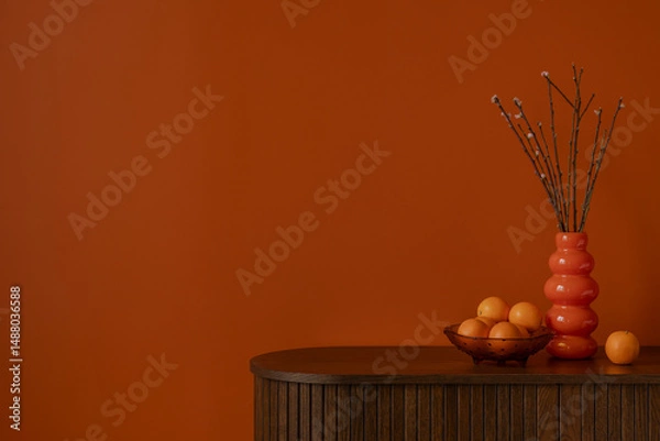 Obraz Bold orange wall with wooden sideboard, sculptural vase, and fresh oranges. Minimalist still life with warm tones and natural textures. Copy space.