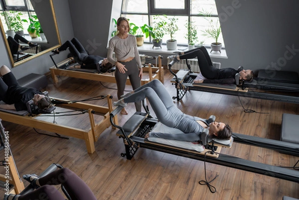 Fototapeta A group of woman exercises Glute bridge on a reformer bed machine in natural sunlight, focusing on pelvis and hips.