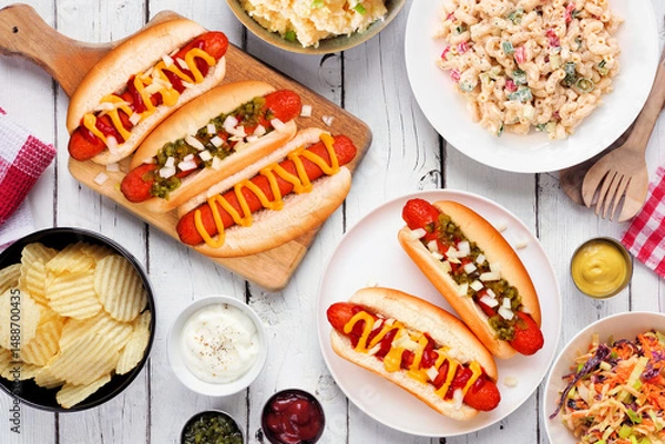 Obraz BBQ table scene with hot dogs, classic salads and snacks. Above view over a white wood background.