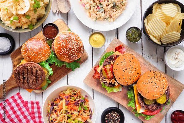 Obraz BBQ table scene with hamburgers, classic salads and snacks. Top down view over a white wood background.