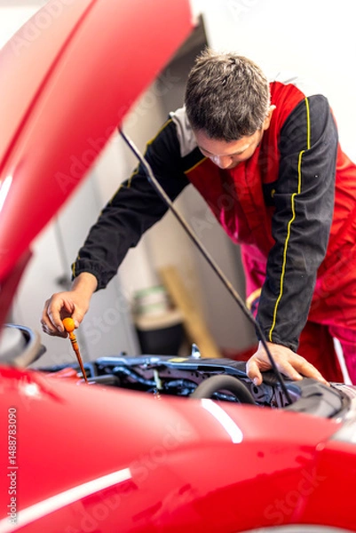 Fototapeta Technician checking dipstick for level oil in engine car in garage. Engine service check, oil dipstick detail in service. Engine problems, engine repair at a car repair shop