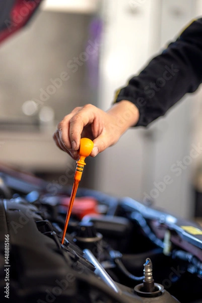 Fototapeta Technician checking dipstick for level oil in engine car in garage. Engine service check, oil dipstick detail in service. Engine problems, engine repair at a car repair shop
