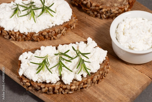 Fototapeta Delicious rye bread topped with creamy cheese and fresh herbs on a rustic wooden board