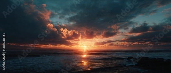 Fototapeta Fiery sunset over the ocean, casting warm hues across the dramatic cloudscape.