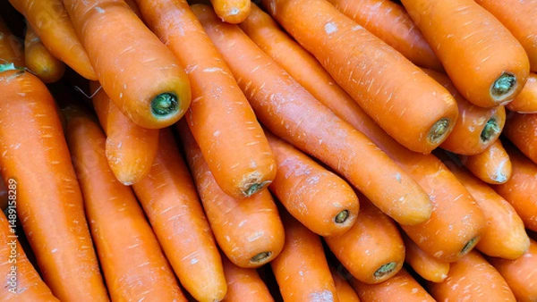 Fototapeta Fresh orange carrots stacked in a market display in vibrant colors for sale at local grocery store