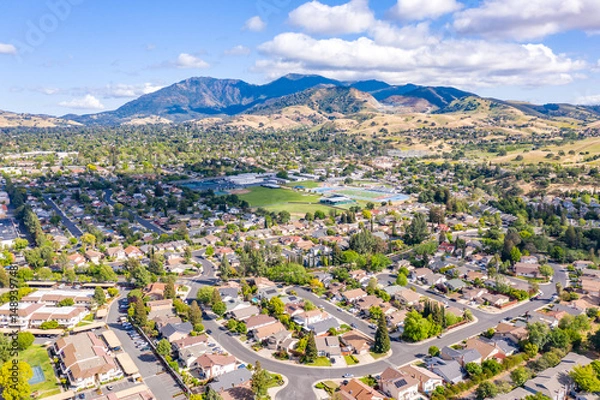 Obraz Aerial drone view of Concord, California, featuring residential neighborhoods, a sports complex, and Mount Diablo in the scenic background under a partly cloudy blue sky.