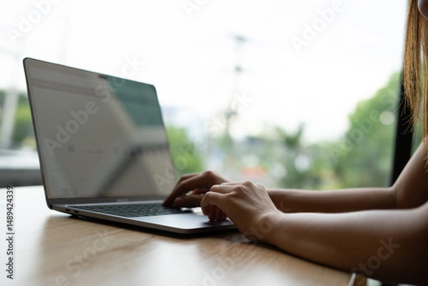 Fototapeta Woman's hands typing on laptop keyboard. Freelance or self-employed woman sitting at wooden desk with phone and smartphone.