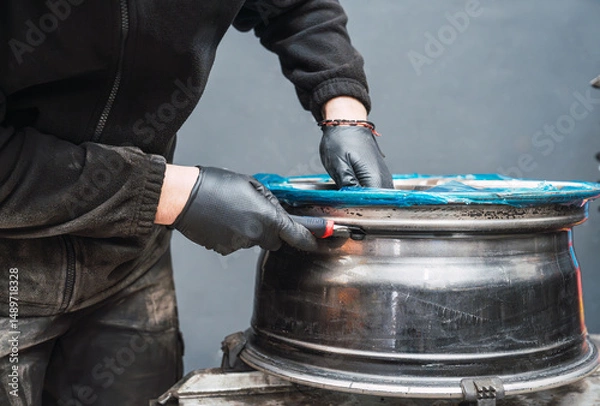 Obraz Mechanic removing protective film from alloy wheel rim in auto repair shop