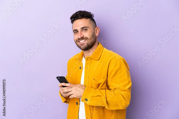 Fototapeta Caucasian man isolated on purple background sending a message or email with the mobile