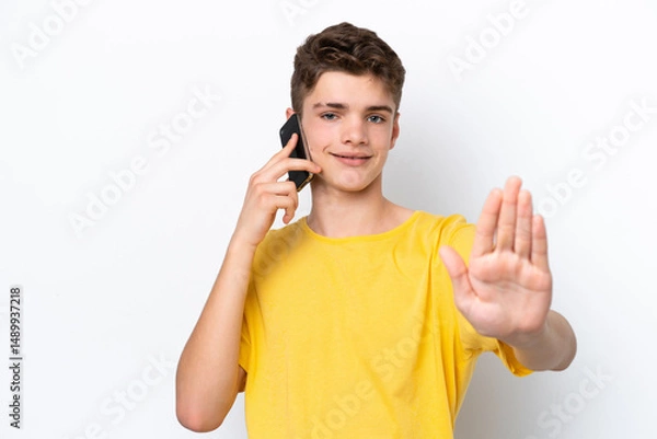 Fototapeta Teenager man using mobile phone isolated on white background making stop gesture