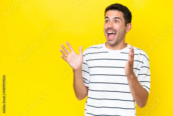 Fototapeta Young handsome man over isolated yellow background with surprise facial expression