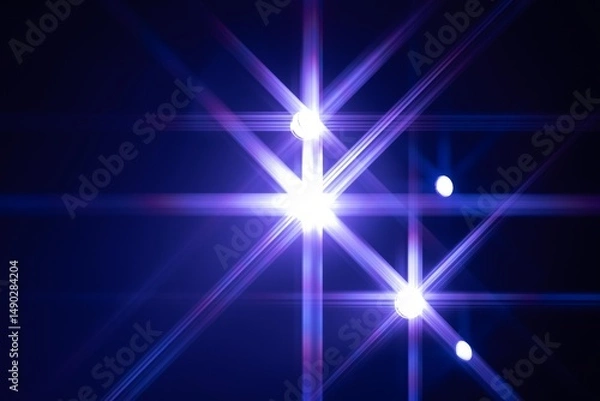 Fototapeta A vibrant display of stage lights emitting blue and violet starburst patterns against a dark background, creating a visually striking abstract composition. Copy space included.