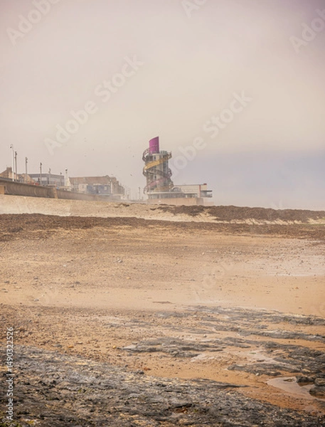 Fototapeta A sea mist clears from a beach and tower is in the background.