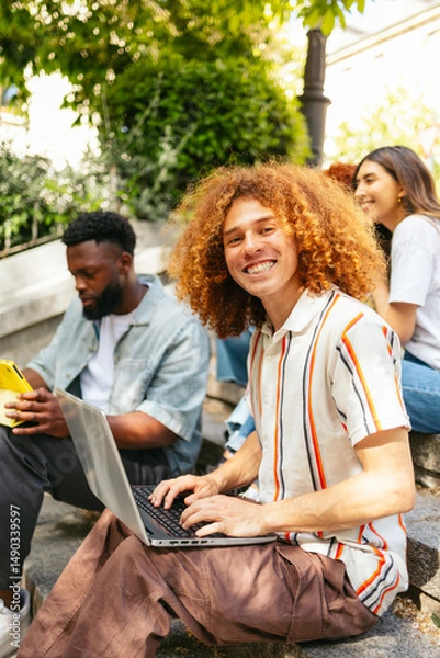 Fototapeta College student using laptop on campus steps with friends