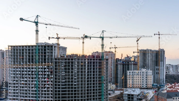 Fototapeta Construction site, cranes and multi-storey unfinished buildings at sunrise or sunset