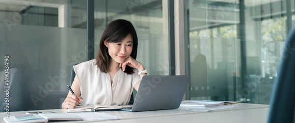 Fototapeta Young businesswoman professional employee using pc doing online banking analysing at workplace. Asian middle-aged business woman working on laptop computer in office, taking notes. Banner, copy space