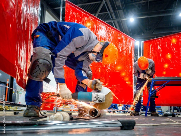 Obraz Two workers in protective gear cutting metal pipes with angle grinders, sparks flying, in a safety-zoned industrial workspace. Metalworking. Grinding. Fabrication. Construction.