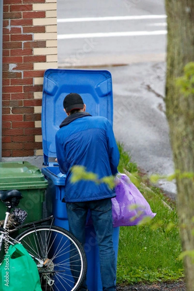 Fototapeta Un homme cherche des bouteilles vides dans les poubelles. Pauvreté urbaine.	