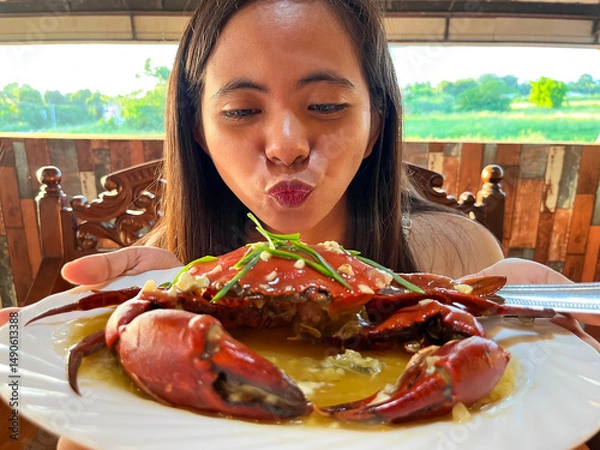 Fototapeta young asian woman showing off crab on plate peeking out from behind crab
