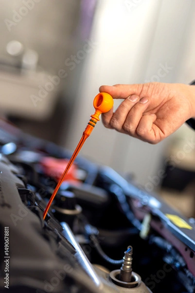 Fototapeta Technician checking dipstick for level oil in engine car in garage. Engine service check, oil dipstick detail in service. Engine problems, engine repair at a car repair shop