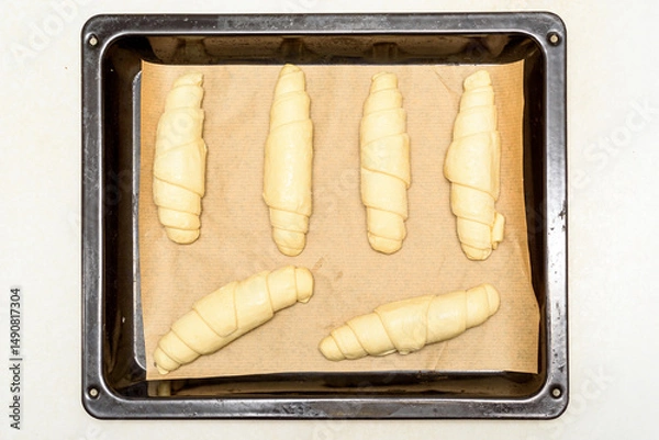 Obraz Top view of uncooked croissants on baking paper and baking sheet.
