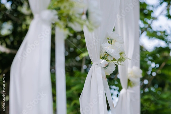 Obraz White flowers with green leaves tied together into a bouquet are attached to white cloth to decorate the wedding aisle, making it look beautiful and simple.	
