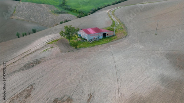 Fototapeta Italy, May 15, 2025: Aerial view of a farmhouse equipped with solar panels in the middle of plowed fields. Peace, tranquility with renewable energy is conveyed by this image

