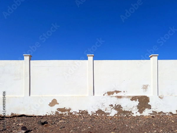 Fototapeta Front view of an old white cement wall under a blue sky. White stone wall. Architecture and Construction