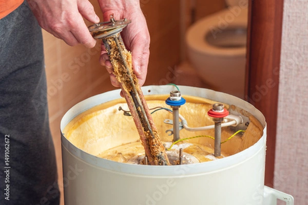 Fototapeta A worker holds a heating element of an electric boiler covered in rust and mineral deposits. Boiler maintenance and repair