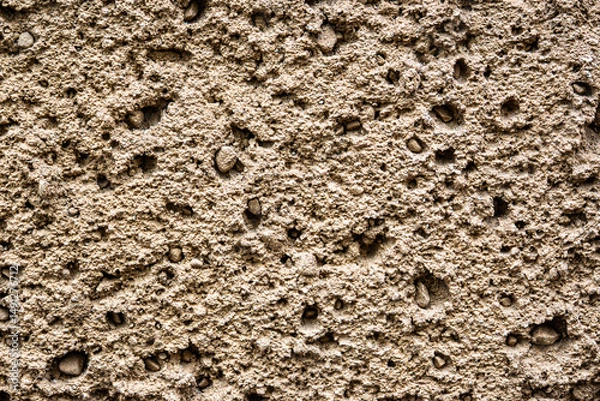 Obraz Detailed close-up of a rough, porous wall texture with uneven surface and embedded pebbles. Ideal for backgrounds, design, or 3D texture mapping.