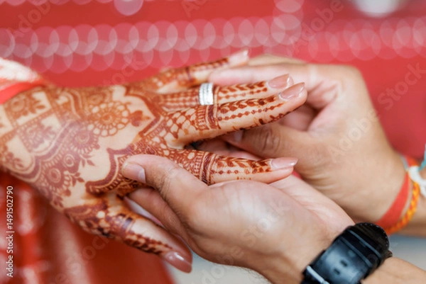Obraz Hands of a bride and groom at an Indian wedding ring exchange ceremony. Groom puts a wedding ring on the finger of the bride with mehendi. Couple exchanging rings on a Hindu engagement ceremony