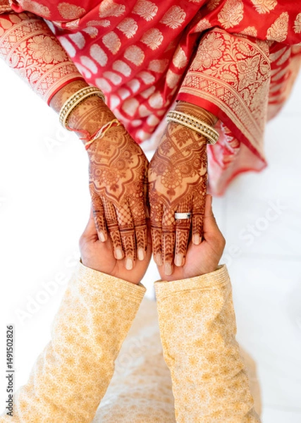 Obraz Hands of a bride and groom in traditional Indian attire close-up. The bride with mehendi henna and gold jewelry holds her hands on the groom's hands. Couple in festive Indian costumes cropped photo