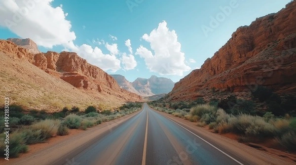 Obraz Scenic road winding through majestic red rock formations under a bright blue sky with fluffy clouds in a serene landscape Generative AI
