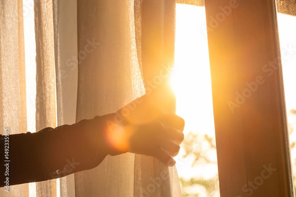 Fototapeta woman's hand She opened the curtains on the window. There was morning light through the window in her room, looking at the view of the mountains and trees as the sun rose	