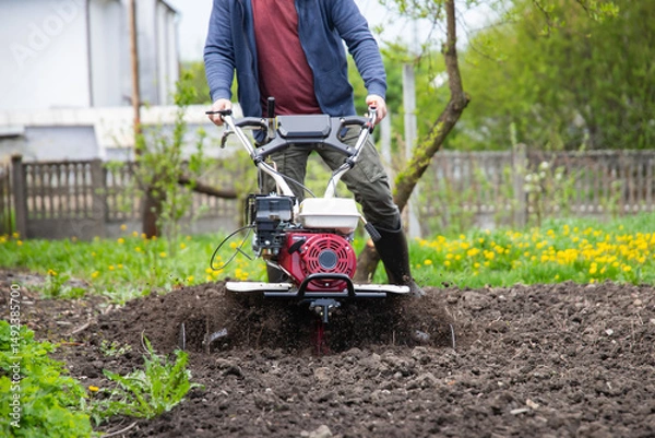 Obraz Farmer using tiller on a plowed field
