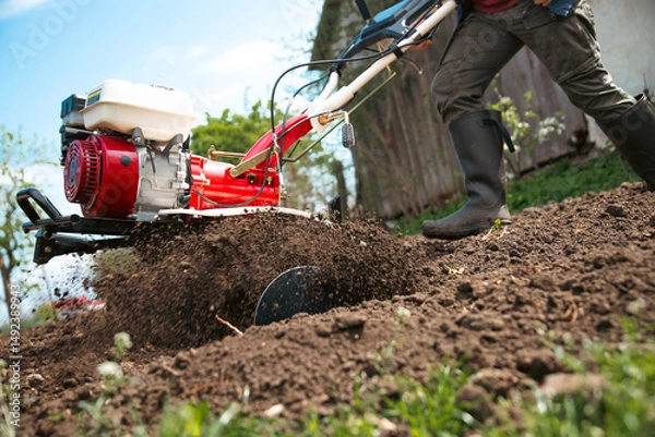 Obraz Farmer using tiller on a plowed field
