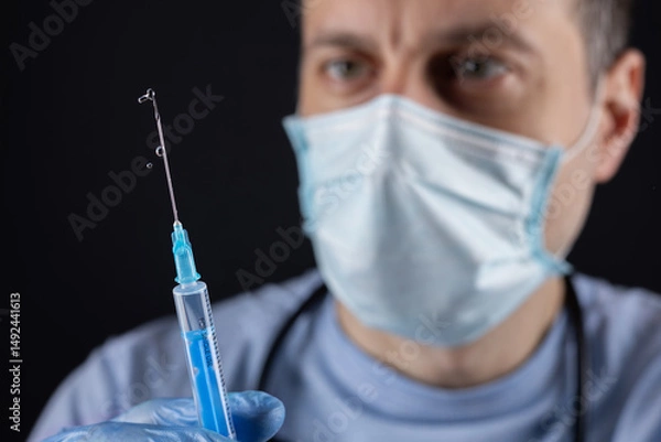 Fototapeta A doctor wearing a mask and gloves measures out the vaccine before administering an injection