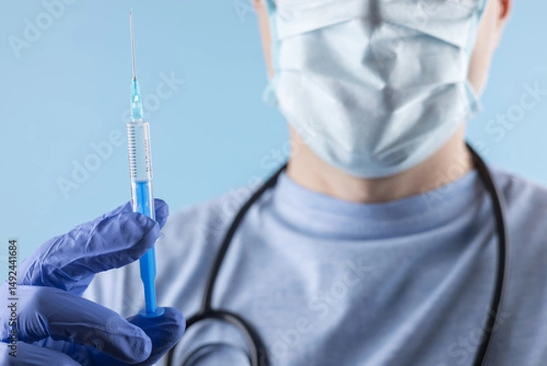 Fototapeta A doctor wearing a mask and gloves measures out the vaccine before administering an injection