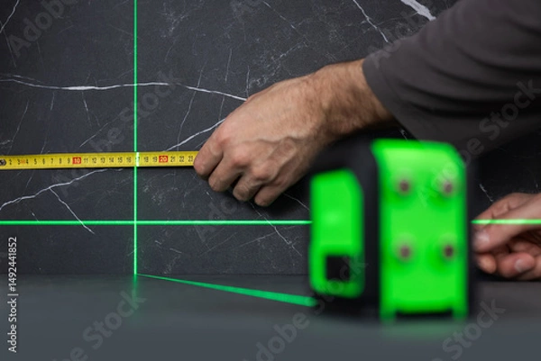 Fototapeta man measuring with tape with green laser level on wall