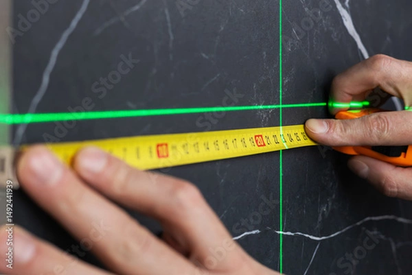 Fototapeta hands of a worker who measures the width of a tabletop with a tape measure and a laser