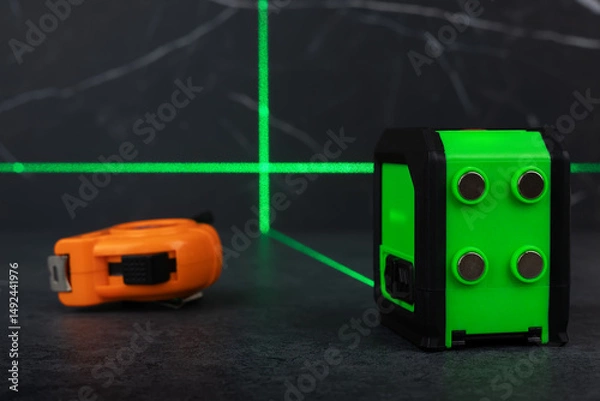 Fototapeta Construction tools, green laser level measurer and tape measure on dark background