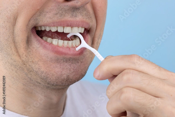 Fototapeta Man brushing teeth with toothpick with dental floss on blue background