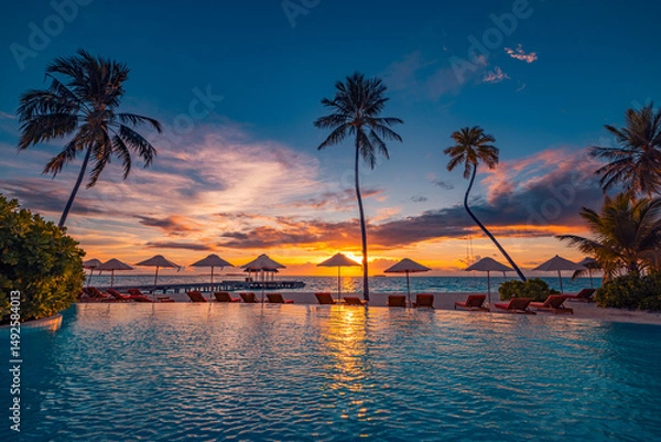 Fototapeta Golden sunset over tranquil beach resort pool palm trees, reflecting warm sunlight on water and seascape. Idyllic tropical escape for relaxation luxury tourism resort vacation. Summer calm landscape