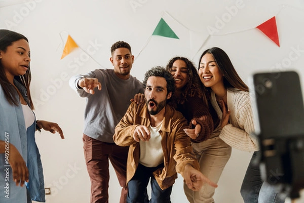 Fototapeta Young brown-skinned male and female friends enthusiastically record an entertaining video with a smartphone, dancing and singing. A concept of partying, togetherness, and friendship.