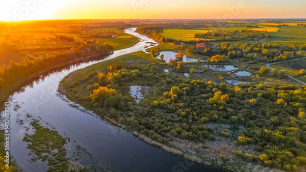 Obraz Aerial view of winding river and wetlands at sunset Drone image showing a meandering river, wetlands, and green landscape illuminated by golden sunset.
