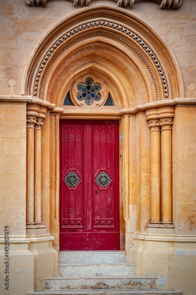 Obraz Traditional arched red door with large doorknobs and rose window. in Mdina, Malta.