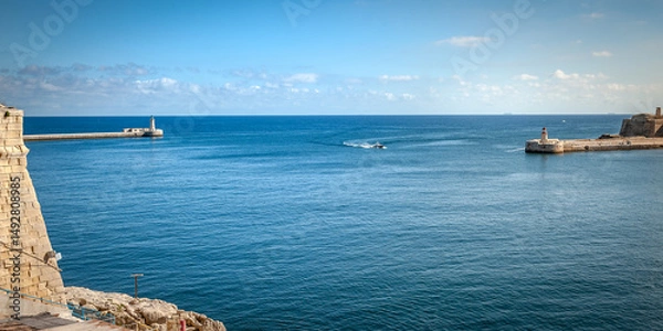 Fototapeta A boat enters the sea gate . Seascape with lighthouses and the walls of the city of Valletta, Malta.