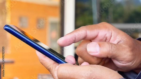 Fototapeta Tapping the Digital Realm: Focused hands skillfully interact with a sleek smartphone, immersed in the realm of digital communication.